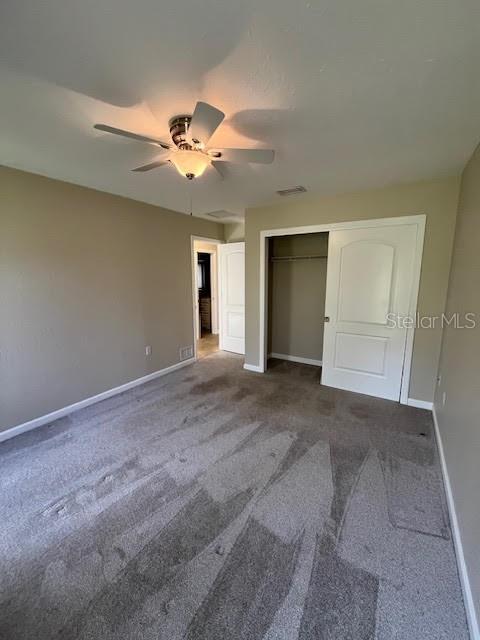 unfurnished bedroom with ceiling fan, dark carpet, and a closet