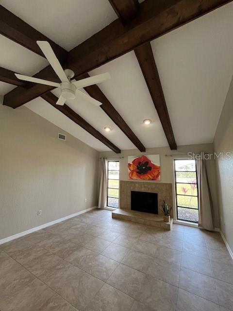 unfurnished living room featuring a tiled fireplace, ceiling fan, lofted ceiling with beams, and a healthy amount of sunlight