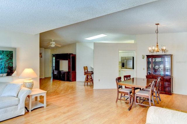 dining space featuring ceiling fan with notable chandelier, a textured ceiling, and light hardwood / wood-style flooring