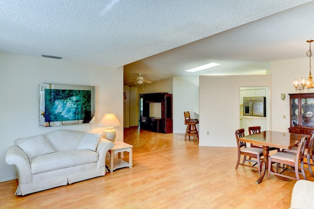 living room with ceiling fan with notable chandelier, light wood-type flooring, and a textured ceiling