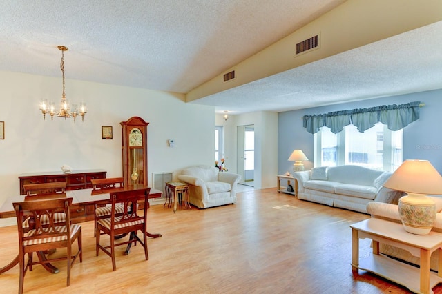 living room featuring a chandelier, a textured ceiling, light hardwood / wood-style floors, and lofted ceiling