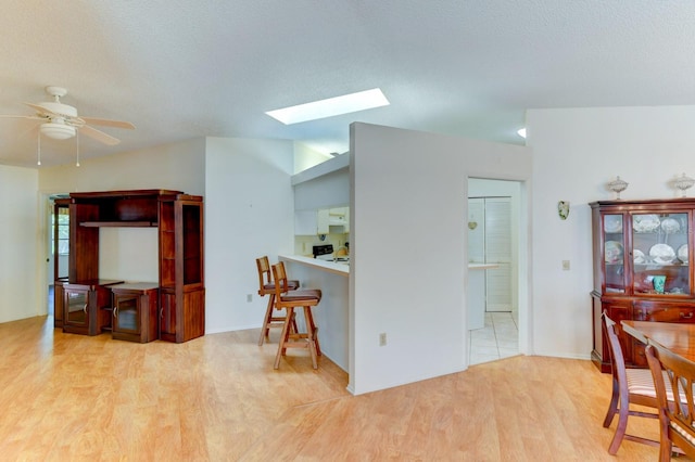 kitchen featuring a textured ceiling, light wood-type flooring, a skylight, and ceiling fan