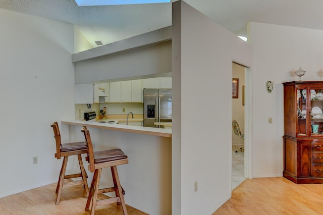 kitchen featuring a skylight, white cabinetry, stainless steel appliances, light hardwood / wood-style flooring, and a breakfast bar area