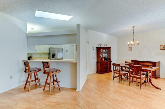 kitchen featuring kitchen peninsula, stainless steel fridge, light wood-type flooring, a skylight, and white cabinets