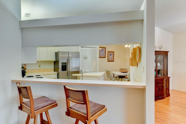 kitchen with white cabinetry, a kitchen breakfast bar, light hardwood / wood-style flooring, kitchen peninsula, and stainless steel fridge