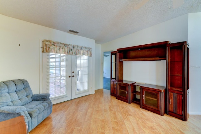 living room featuring light wood-type flooring, a textured ceiling, and french doors