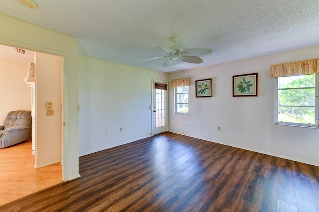 empty room with ceiling fan, plenty of natural light, dark wood-type flooring, and a textured ceiling