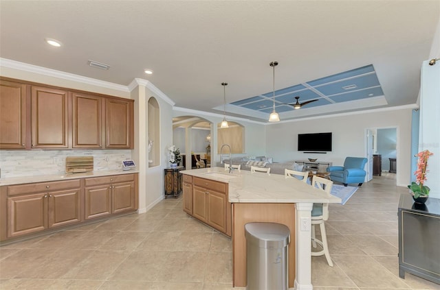 kitchen with backsplash, a kitchen island with sink, a raised ceiling, sink, and ceiling fan