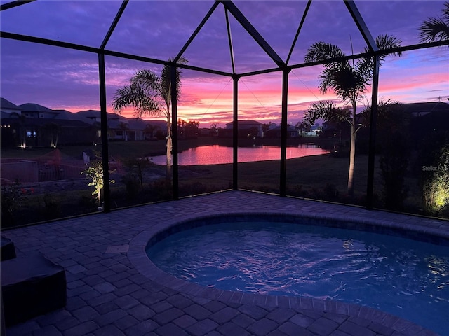 pool at dusk featuring a lanai, a water view, and a patio