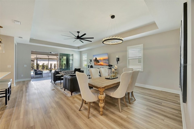 dining room with light wood-type flooring, a raised ceiling, and ceiling fan