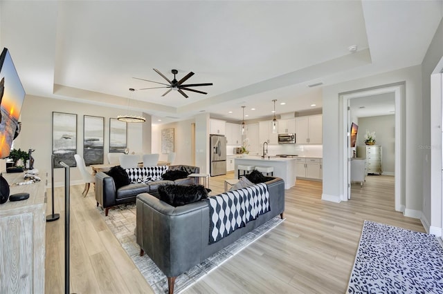 living room with light hardwood / wood-style floors, ceiling fan, a tray ceiling, and sink