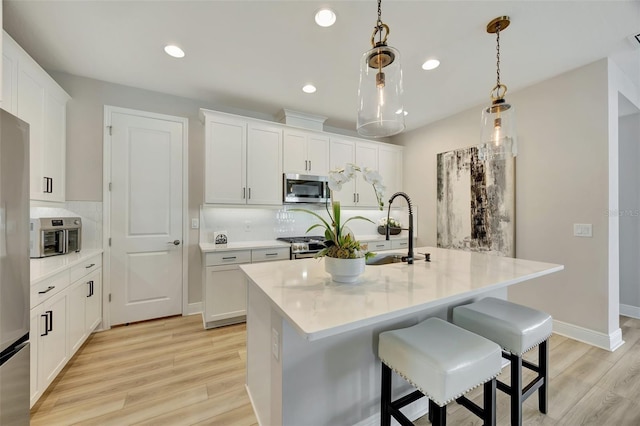 kitchen featuring appliances with stainless steel finishes, light wood-type flooring, sink, white cabinetry, and hanging light fixtures