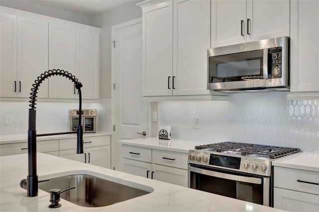 kitchen featuring white cabinetry, sink, light stone counters, decorative backsplash, and appliances with stainless steel finishes