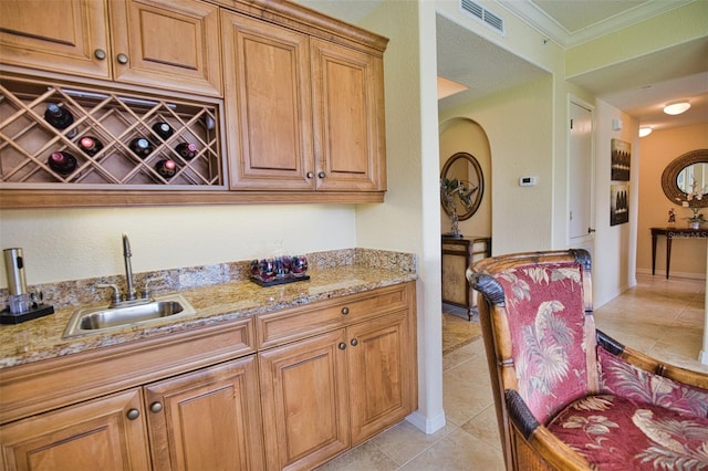 kitchen with light stone countertops, light tile patterned floors, crown molding, and sink