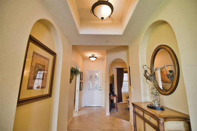 hall featuring a raised ceiling, light tile patterned floors, and a textured ceiling