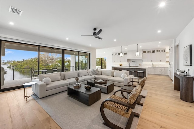 living room featuring a wealth of natural light, light hardwood / wood-style flooring, a water view, and ceiling fan