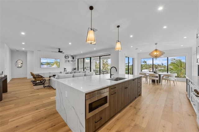 kitchen with stainless steel microwave, light stone counters, sink, and light hardwood / wood-style flooring