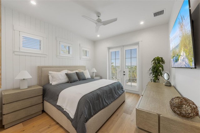 bedroom featuring french doors, wooden walls, light hardwood / wood-style flooring, ceiling fan, and access to exterior