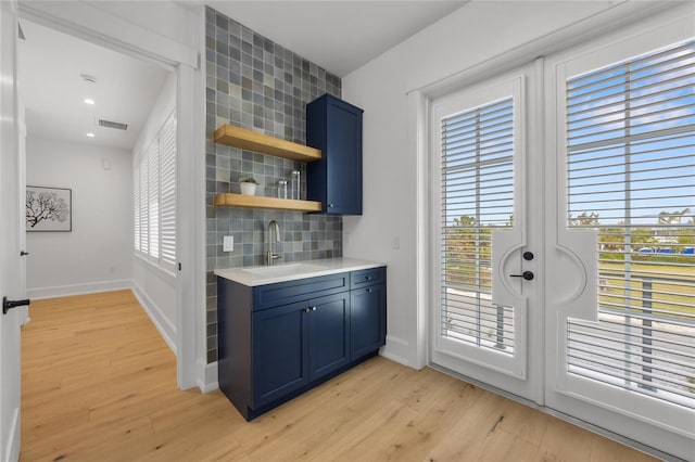 bar featuring a wealth of natural light, sink, blue cabinets, and light wood-type flooring