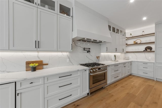 kitchen featuring white cabinets, decorative backsplash, stainless steel stove, and premium range hood