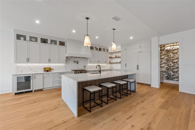 kitchen with white cabinetry, wine cooler, light hardwood / wood-style flooring, an island with sink, and custom range hood