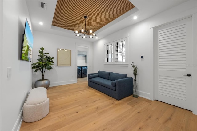 living area featuring a tray ceiling, washer and clothes dryer, an inviting chandelier, and light wood-type flooring