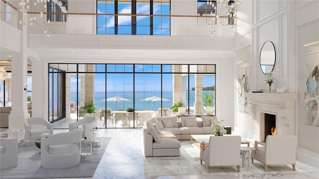 living room featuring a towering ceiling, a chandelier, a water view, and a fireplace