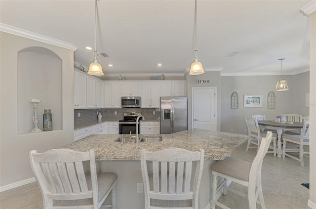 kitchen featuring white cabinetry, a center island with sink, appliances with stainless steel finishes, decorative light fixtures, and sink