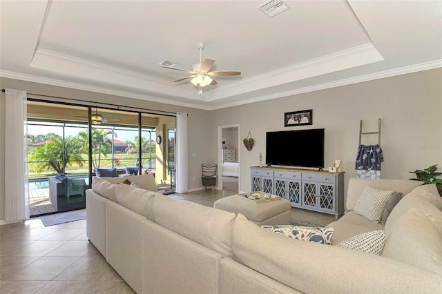 tiled living room with a raised ceiling, ornamental molding, and ceiling fan