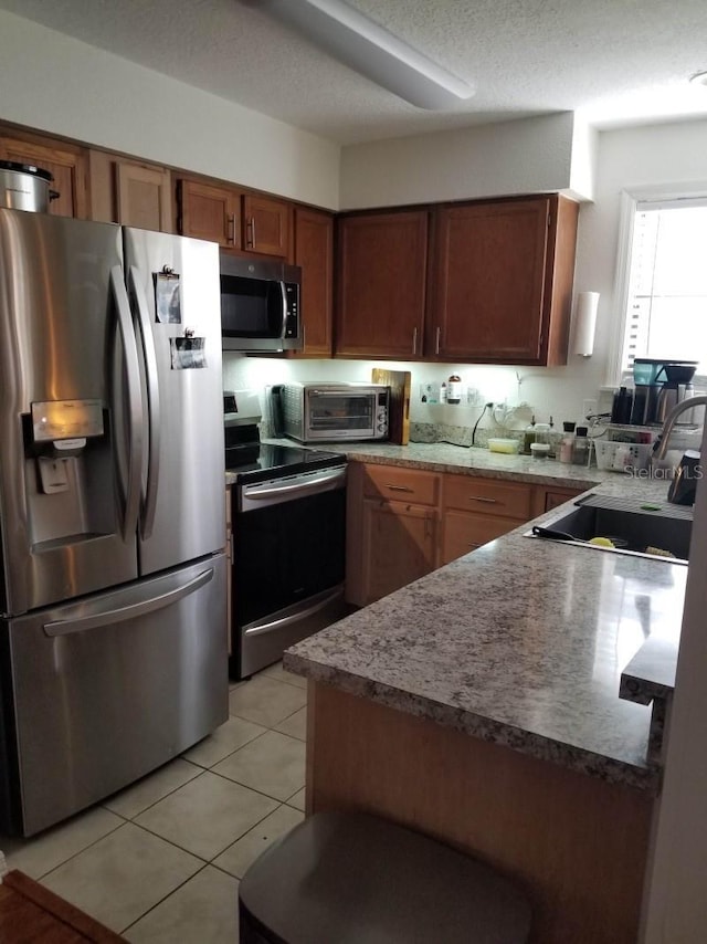 kitchen with a toaster, brown cabinets, stainless steel appliances, a sink, and light tile patterned flooring