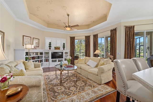 living room with wood-type flooring, a raised ceiling, ceiling fan, and ornamental molding