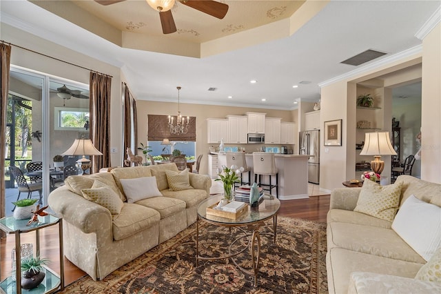 living room with dark hardwood / wood-style flooring, a raised ceiling, crown molding, and a notable chandelier