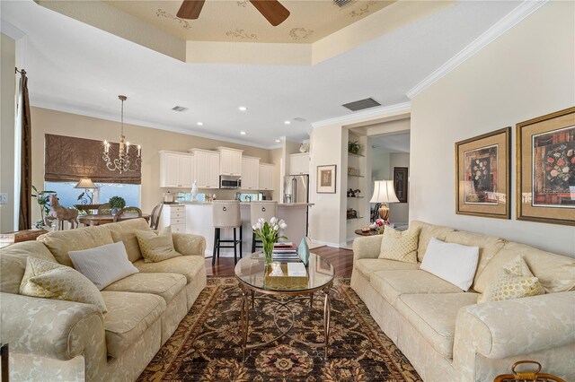 living room featuring a raised ceiling, wood-type flooring, ceiling fan with notable chandelier, and ornamental molding