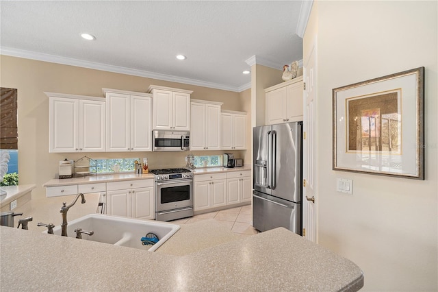 kitchen with sink, light tile patterned floors, ornamental molding, appliances with stainless steel finishes, and white cabinetry