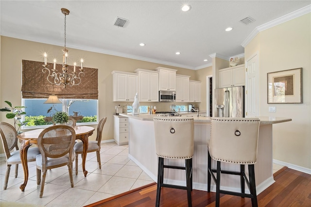 kitchen featuring appliances with stainless steel finishes, light wood-type flooring, a kitchen island with sink, and ornamental molding