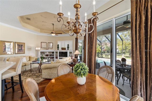 dining space with hardwood / wood-style floors, a raised ceiling, crown molding, and an inviting chandelier