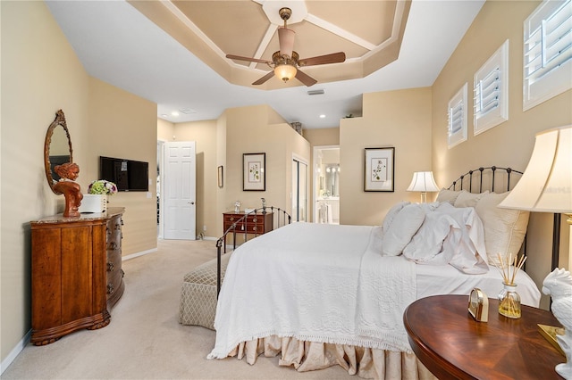 carpeted bedroom featuring connected bathroom, a tray ceiling, and ceiling fan