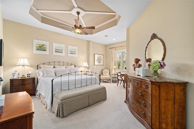 bedroom with ceiling fan, light carpet, and a tray ceiling