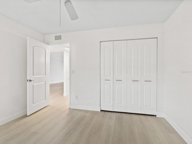 unfurnished bedroom with a textured ceiling, a closet, light hardwood / wood-style flooring, and ceiling fan