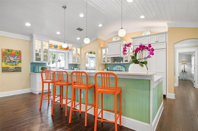 kitchen with pendant lighting, backsplash, white cabinetry, and vaulted ceiling