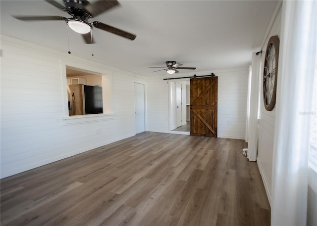 unfurnished room featuring ceiling fan, a barn door, and wood-type flooring