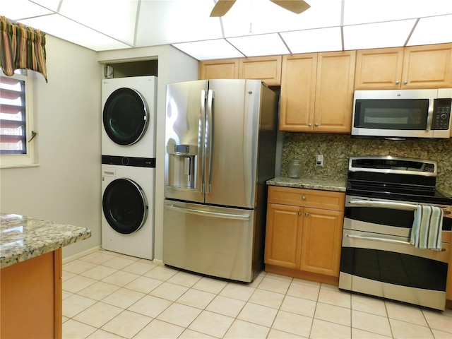 kitchen featuring light stone countertops, ceiling fan, stainless steel appliances, backsplash, and stacked washer and clothes dryer