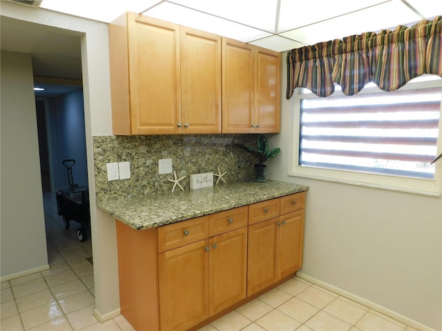 kitchen featuring a paneled ceiling, decorative backsplash, light tile patterned flooring, and light stone countertops