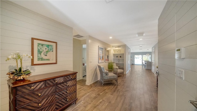 hallway with built in shelves, wooden walls, and light hardwood / wood-style flooring