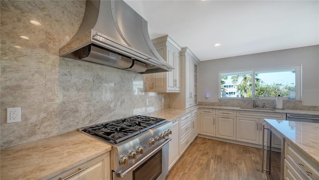 kitchen featuring light stone countertops, tasteful backsplash, premium range hood, high end stove, and light hardwood / wood-style floors