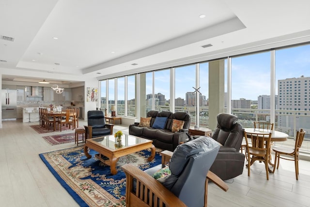 living room with light wood-type flooring and a raised ceiling