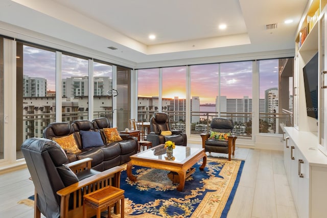 living room with light hardwood / wood-style floors, a raised ceiling, and a healthy amount of sunlight