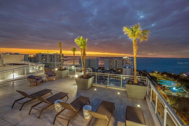 patio terrace at dusk featuring a water view and a balcony