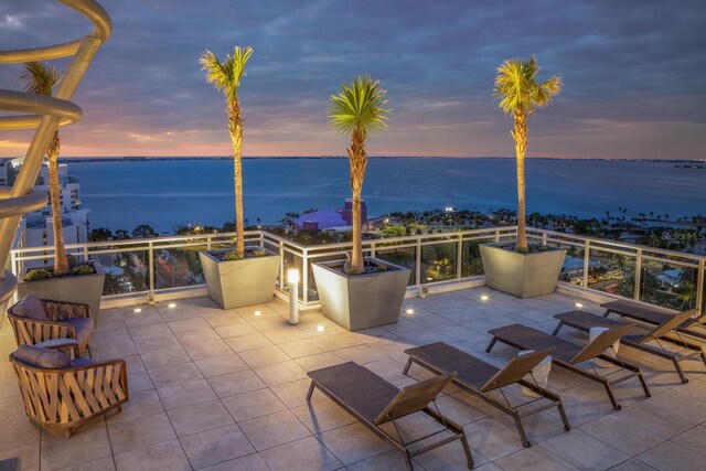 patio terrace at dusk featuring a water view and a balcony