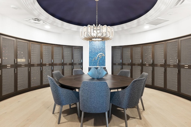 dining room with a notable chandelier, a raised ceiling, and light wood-type flooring